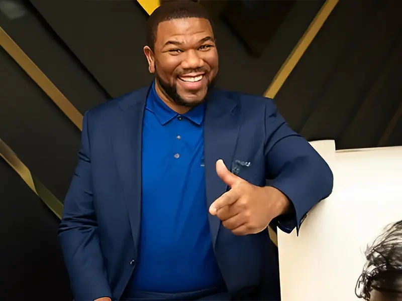 A man in a blue shirt and jacket smiling.