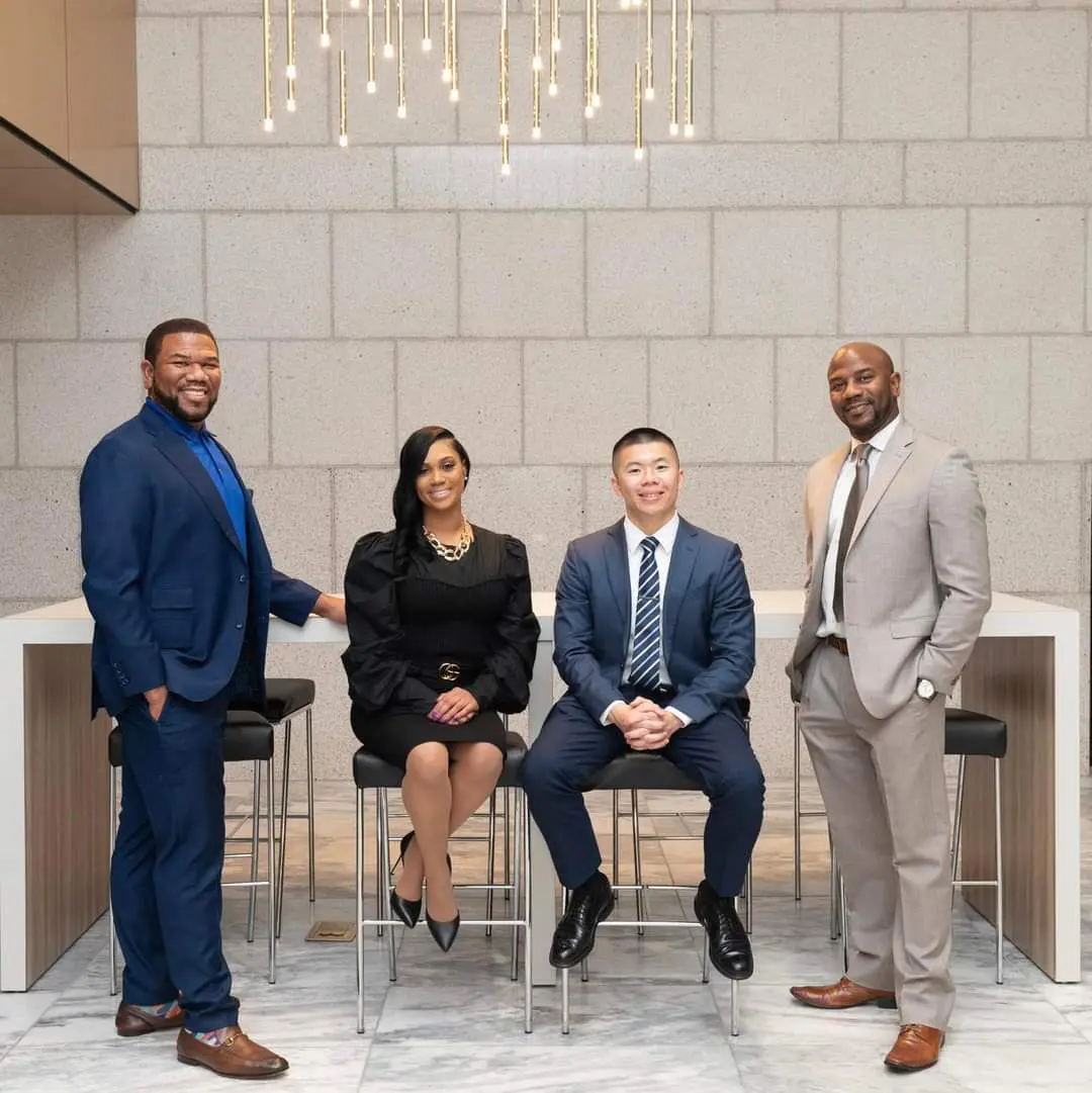 Four people in suits and ties sitting on stools.